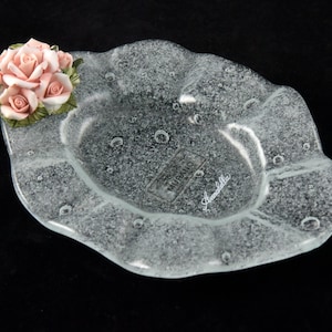 May include: A clear glass dish with a textured surface and a raised edge. The dish has a floral design on the side and the text "MURANO" and "Annalisa" on the bottom.