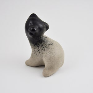 May include: A small ceramic sculpture of a bear, painted in black and white. The bear is sitting up and looking to the side.