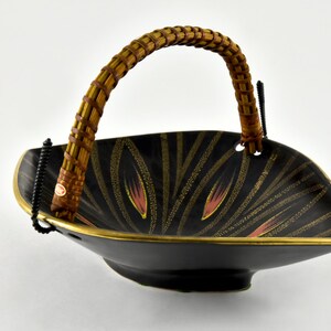 May include: A black ceramic serving bowl with a gold rim and a woven bamboo handle. The bowl has a geometric design with gold and red accents.