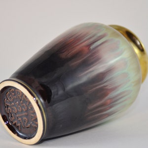 May include: A brown and green ceramic vase with a gold rim. The vase has a unique, marbled glaze and a brown base with the text "GERMAN 2333 712" stamped on it.