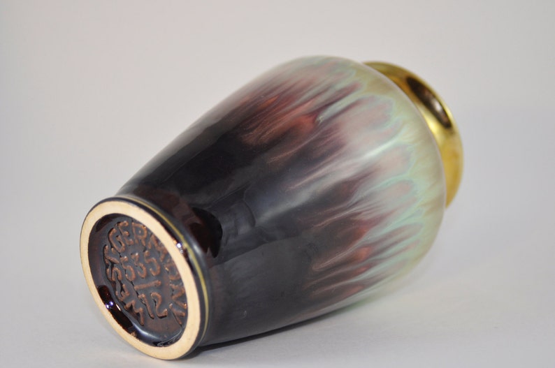 May include: A brown and green ceramic vase with a gold rim. The vase has a unique, marbled glaze and a brown base with the text "GERMAN 2333 712" stamped on it.