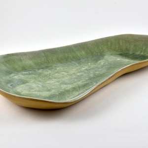 May include: A long, green ceramic serving dish with a slightly wavy edge and a yellow rim. The dish has a mottled, textured surface.