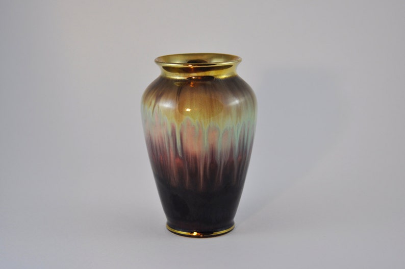 May include: A ceramic vase with a gold rim and a gradient of colours from dark purple to light green.