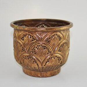 Peut inclure: Un pot de fleurs décoratif en métal doré avec un motif floral complexe. Le pot a une forme ronde et une base large.