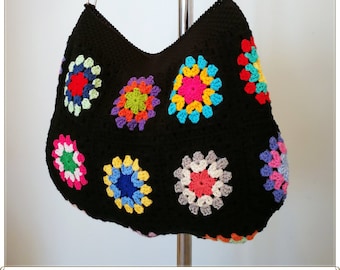 May include: A black crocheted shoulder bag with colorful granny square motifs. The bag has a long black strap and is hanging from a metal stand.