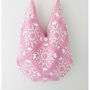 Può includere: Una borsa a tracolla in stile hobo realizzata in filato lavorato all'uncinetto rosa e bianco con un motivo quadrato. La borsa presenta una singola tracolla, una chiusura con bottone bianco al centro e una fodera in tessuto bianco.