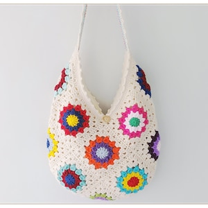 May include: A white crocheted tote bag with colorful granny square motifs. The bag has a single button closure and two long straps.