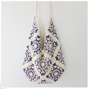 May include: A white crocheted tote bag with a blue floral pattern. The bag has a single button closure and a long strap.