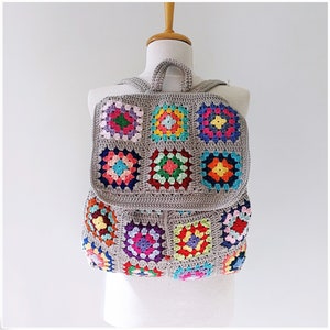 Pu&ograve; includere: Uno zaino in crochet grigio con toppe quadrate colorate. Lo zaino ha un manico superiore e spalline regolabili.