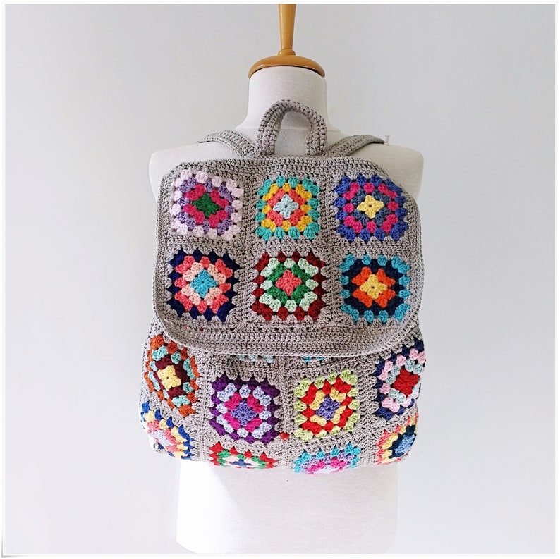 Pu&ograve; includere: Uno zaino in crochet grigio con toppe quadrate colorate. Lo zaino ha un manico superiore e spalline regolabili.
