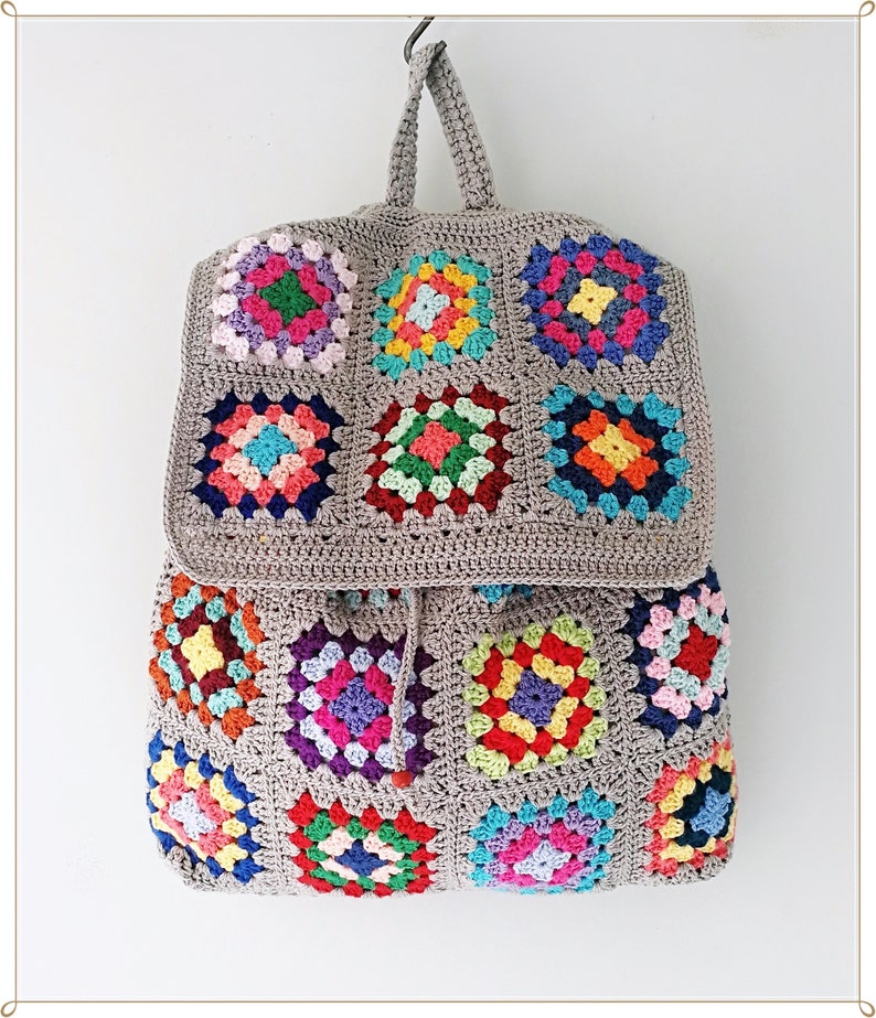 Pu&ograve; includere: Uno zaino in crochet grigio con toppe colorate a quadrato della nonna. Lo zaino ha una chiusura a coulisse e un manico superiore.