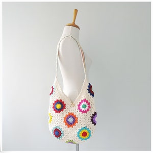 May include: A white crocheted tote bag with a colorful granny square pattern. The bag has a long strap and is perfect for carrying everyday essentials.