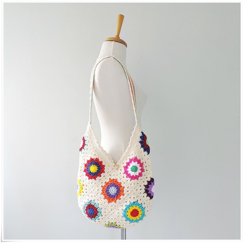 May include: A white crocheted tote bag with a colorful granny square pattern. The bag has a long strap and is perfect for carrying everyday essentials.