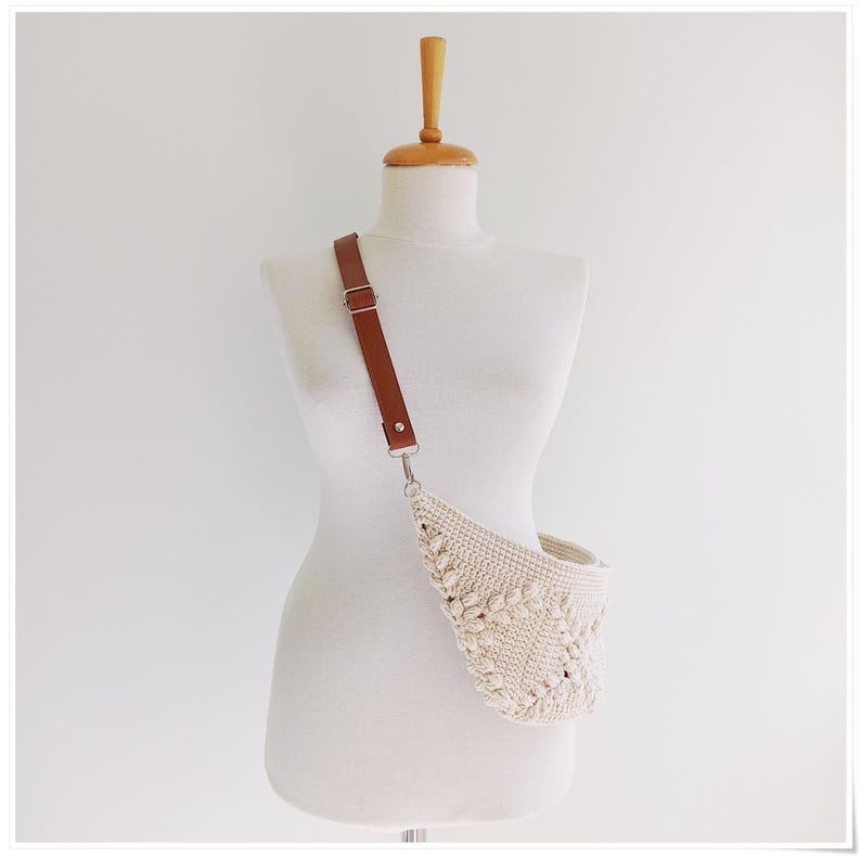 May include: A white crocheted fanny pack with a brown leather strap. The bag is worn on a white mannequin.