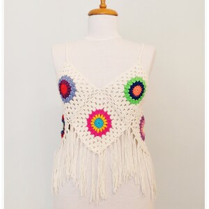 Puede incluir: Top blanco de crochet con detalles florales coloridos y ribete de flecos.