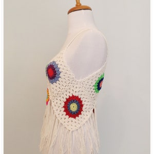 Puede incluir: Top blanco de crochet con dise&ntilde;os florales coloridos y ribete de flecos.