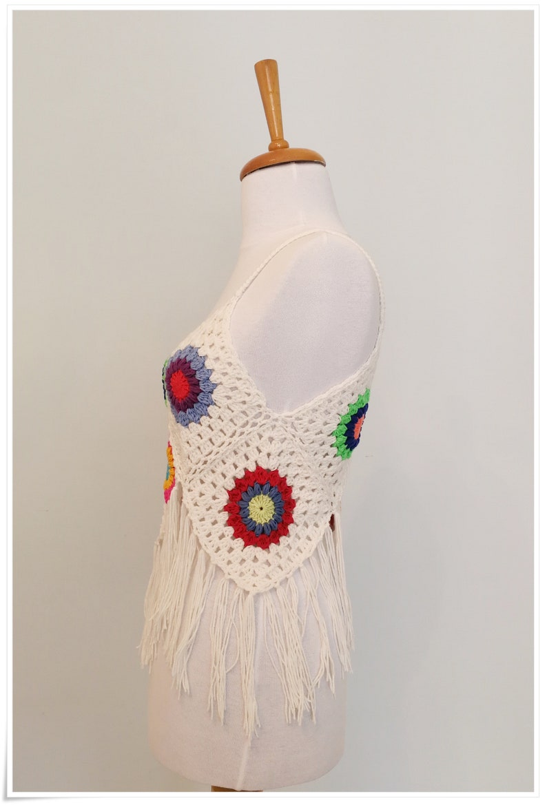 Puede incluir: Top blanco de crochet con dise&ntilde;os florales coloridos y ribete de flecos.