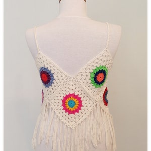 Puede incluir: Top blanco de crochet con detalles florales coloridos y ribete de flecos.