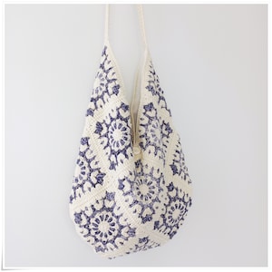 Puede incluir: Un bolso tote de crochet blanco con un patr&oacute;n floral azul. El bolso tiene una correa larga y est&aacute; hecho de un material suave y ligero.