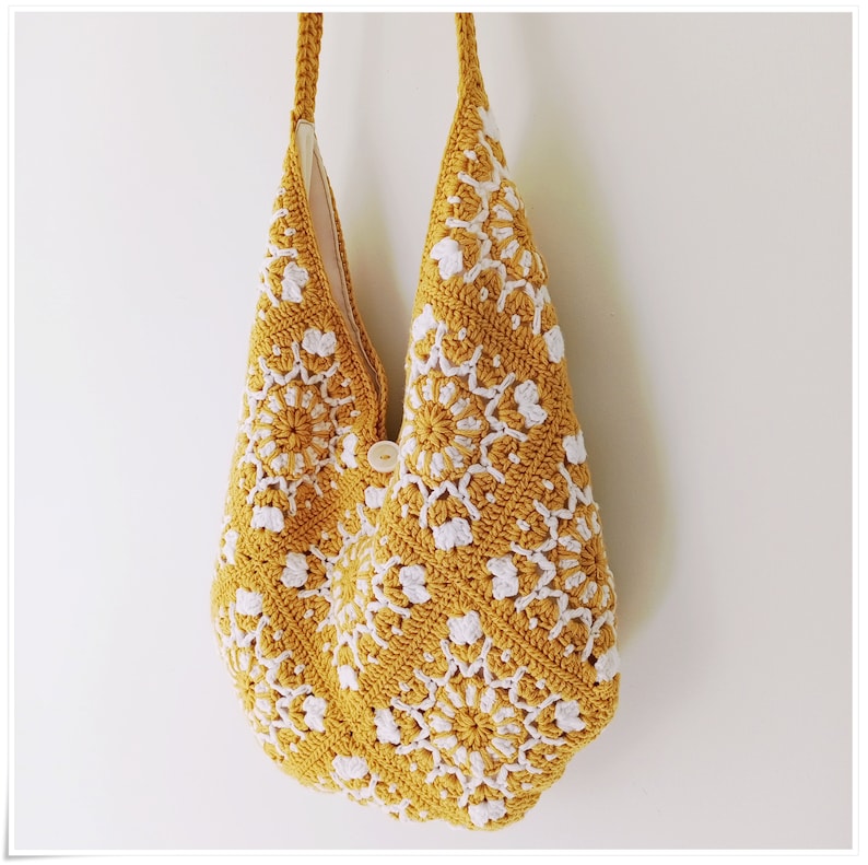 Puede incluir: Una bolsa de mano de crochet amarilla con dise&ntilde;os florales blancos. La bolsa tiene un cierre de bot&oacute;n &uacute;nico.