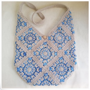 May include: A crocheted beige and blue shoulder bag with a wooden button closure. The bag is made of a square pattern with a circular design in the center of each square.