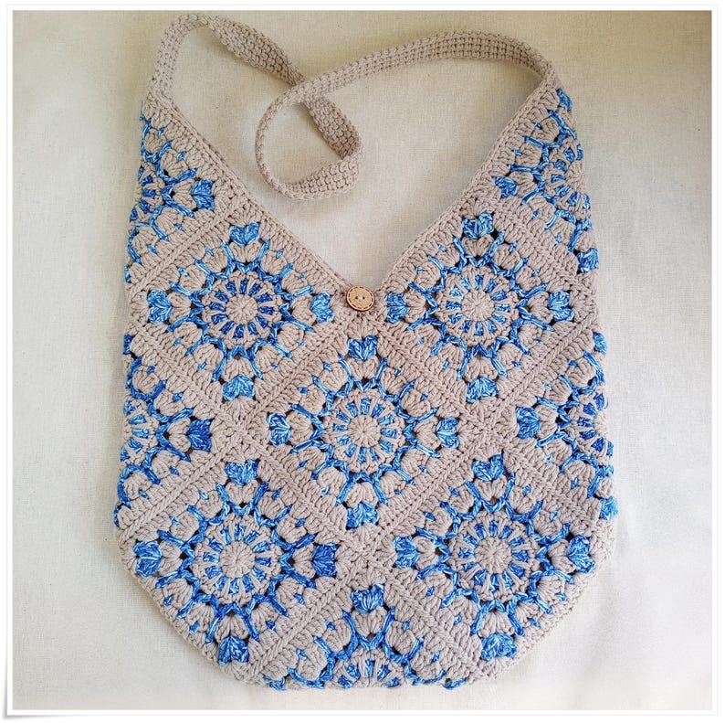 May include: A crocheted beige and blue shoulder bag with a wooden button closure. The bag is made of a square pattern with a circular design in the center of each square.