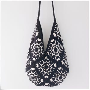 May include: Black and white crocheted tote bag with a floral pattern. The bag has a long strap and is made of a soft, textured material.