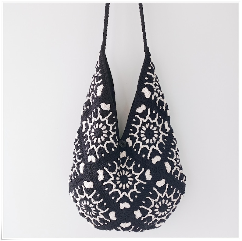 May include: Black and white crocheted tote bag with a floral pattern. The bag has a long strap and is made of a soft, textured material.