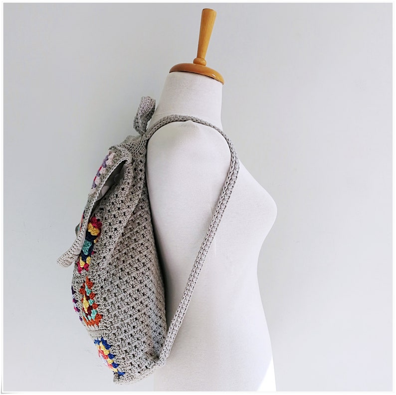Pu&ograve; includere: Uno zaino in crochet grigio con motivi geometrici colorati. Lo zaino ha spalline regolabili e un ampio scomparto principale.