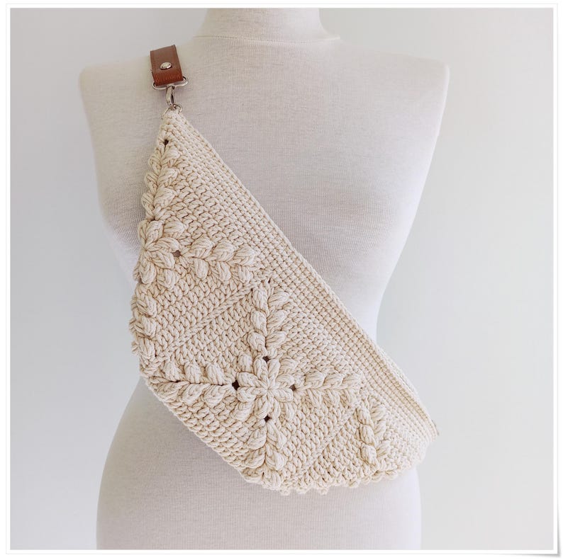 May include: A cream-colored crocheted crossbody bag with a brown leather strap. The bag has a unique floral design.