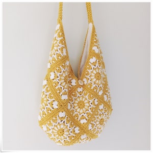 Puede incluir: Una bolsa de mano de crochet amarilla con dise&ntilde;os florales blancos. La bolsa tiene un cierre de bot&oacute;n &uacute;nico y una correa larga.