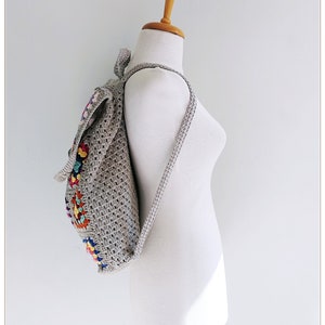 Pu&ograve; includere: Uno zaino in crochet grigio con disegni quadrati colorati. Lo zaino ha spalline regolabili e una chiusura a coulisse.