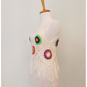 Puede incluir: Top blanco de crochet con dise&ntilde;os florales coloridos y ribete de flecos.