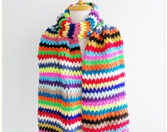 Pode incluir: Uma echarpe de crochê listrada colorida com uma variedade de cores brilhantes, incluindo vermelho, laranja, amarelo, verde, azul, roxo e rosa.