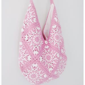 May include: A pink and white crocheted tote bag with a single button closure. The bag is made with a repeating floral pattern.
