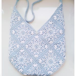 May include: A light blue crocheted tote bag with a white floral pattern. The bag has a single strap and a button closure.