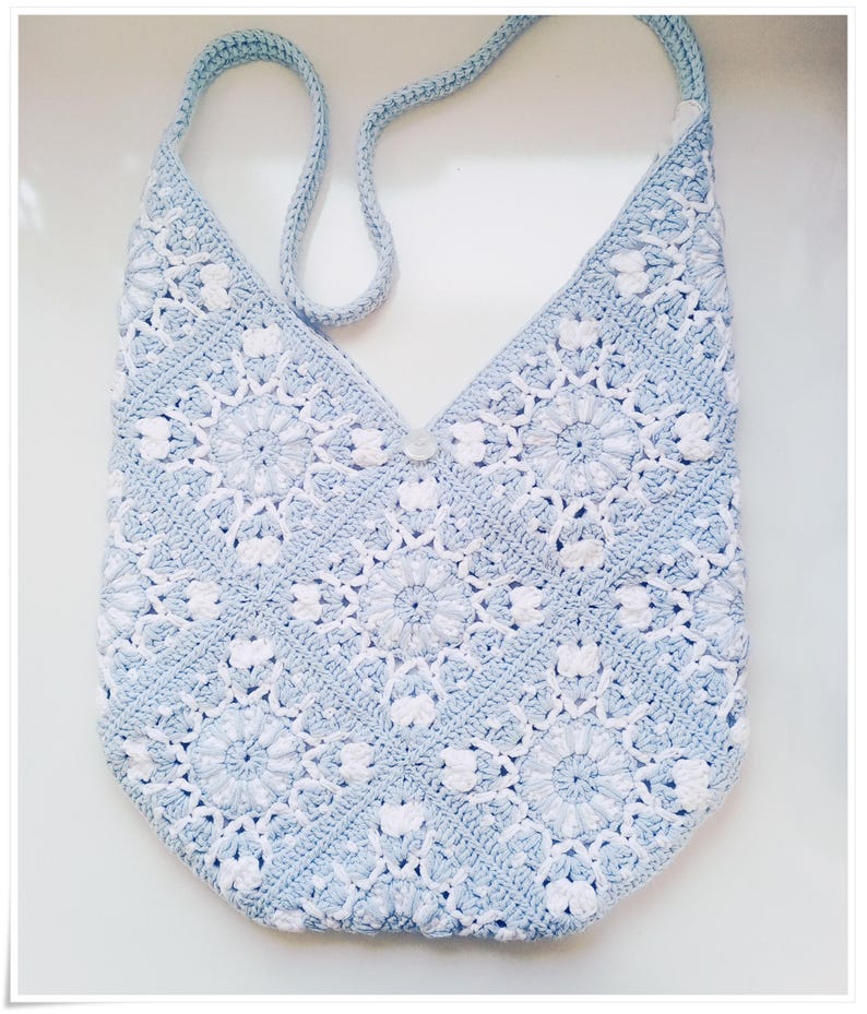 May include: A light blue crocheted tote bag with a white floral pattern. The bag has a single strap and a button closure.