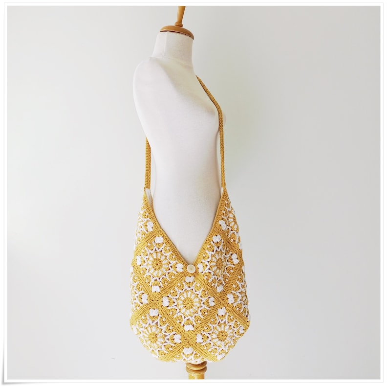 Puede incluir: Un bolso de hombro de crochet amarillo y blanco con cierre de bot&oacute;n. El bolso est&aacute; hecho de un patr&oacute;n cuadrado con un dise&ntilde;o floral.