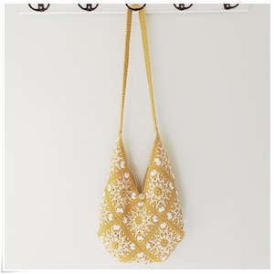 Puede incluir: Un bolso de hombro de crochet amarillo con detalles florales blancos. El bolso tiene una correa larga y un cierre de bot&oacute;n.