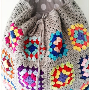 Pu&ograve; includere: Una borsa a cordoncino di uncinetto grigia con una fodera a pois grigi e bianchi. La borsa &egrave; decorata con quadrati di granny colorati.