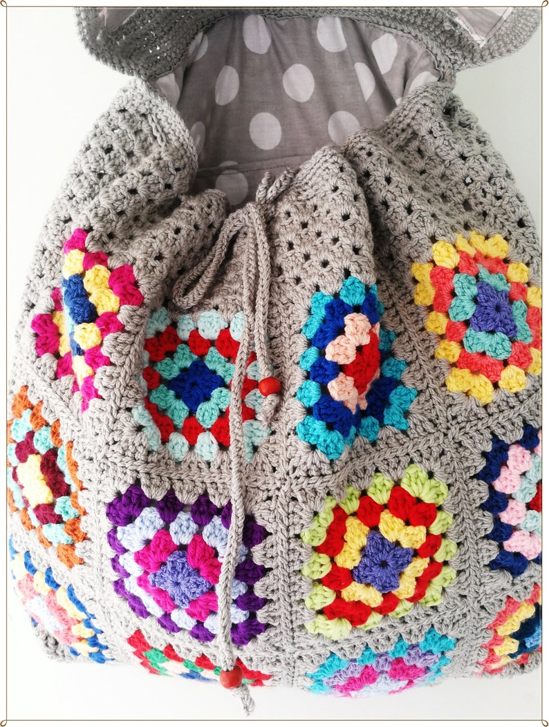 Pu&ograve; includere: Una borsa a cordoncino di uncinetto grigia con una fodera a pois grigi e bianchi. La borsa &egrave; decorata con quadrati di granny colorati.