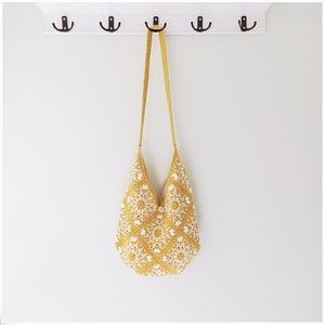 Puede incluir: Un bolso tote de crochet amarillo y blanco con una correa larga colgando de un gancho.