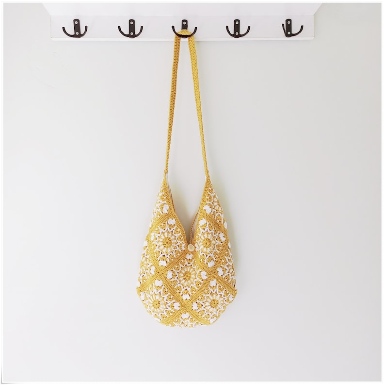 Puede incluir: Un bolso tote de crochet amarillo y blanco con una correa larga colgando de un gancho.