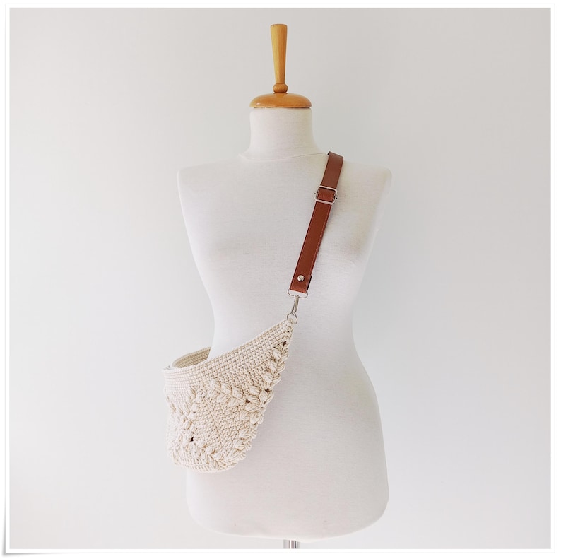 May include: A white crocheted crossbody bag with a brown leather strap. The bag has a unique, textured design.