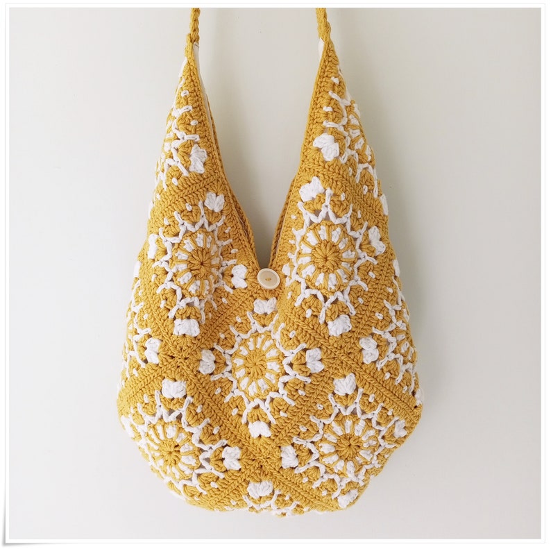 Puede incluir: Un bolso tote de crochet con un patr&oacute;n geom&eacute;trico amarillo y blanco. El bolso tiene un cierre de bot&oacute;n &uacute;nico.
