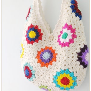 May include: A white crocheted tote bag with colorful granny squares. The squares feature a variety of colors, including red, blue, yellow, green, and purple.