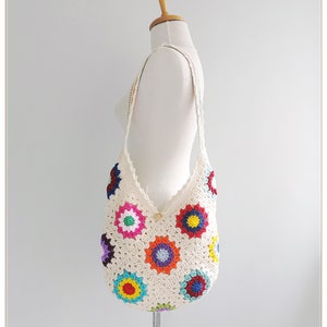 May include: White crochet tote bag with a colorful floral design. The bag has a long strap and is made with a granny square pattern.