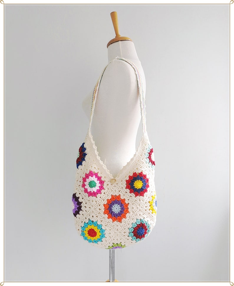 May include: White crochet tote bag with a colorful floral design. The bag has a long strap and is made with a granny square pattern.