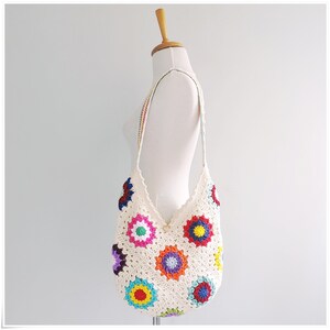 May include: A white crochet shoulder bag with a colorful granny square pattern. The bag has a long strap and is made of cotton yarn.