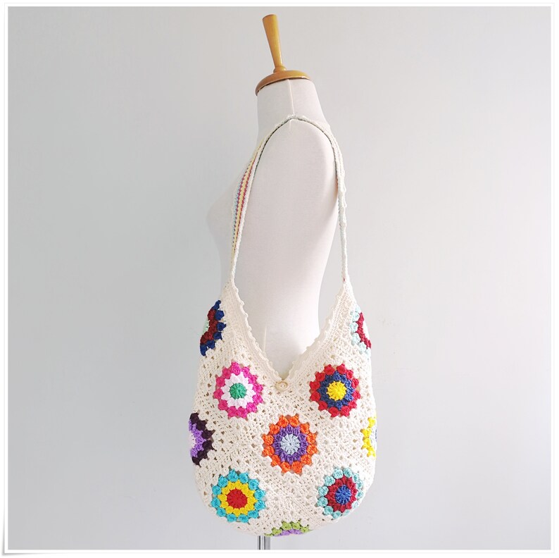 May include: A white crochet shoulder bag with a colorful granny square pattern. The bag has a long strap and is made of cotton yarn.
